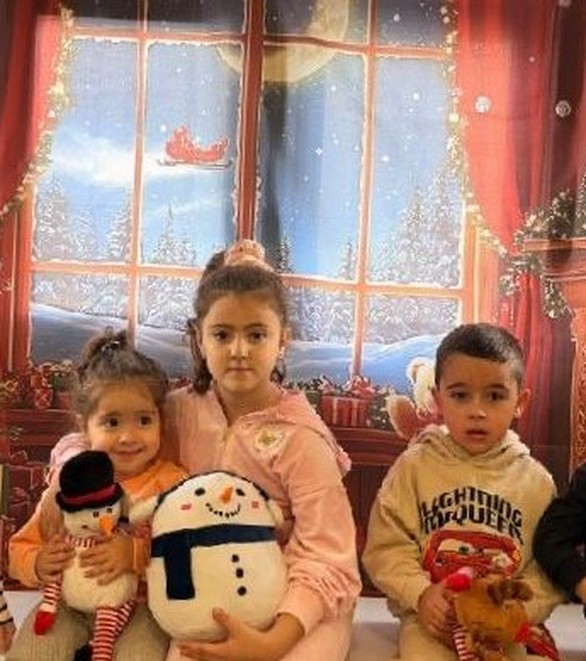 Children posing by a festive window display with a snowman